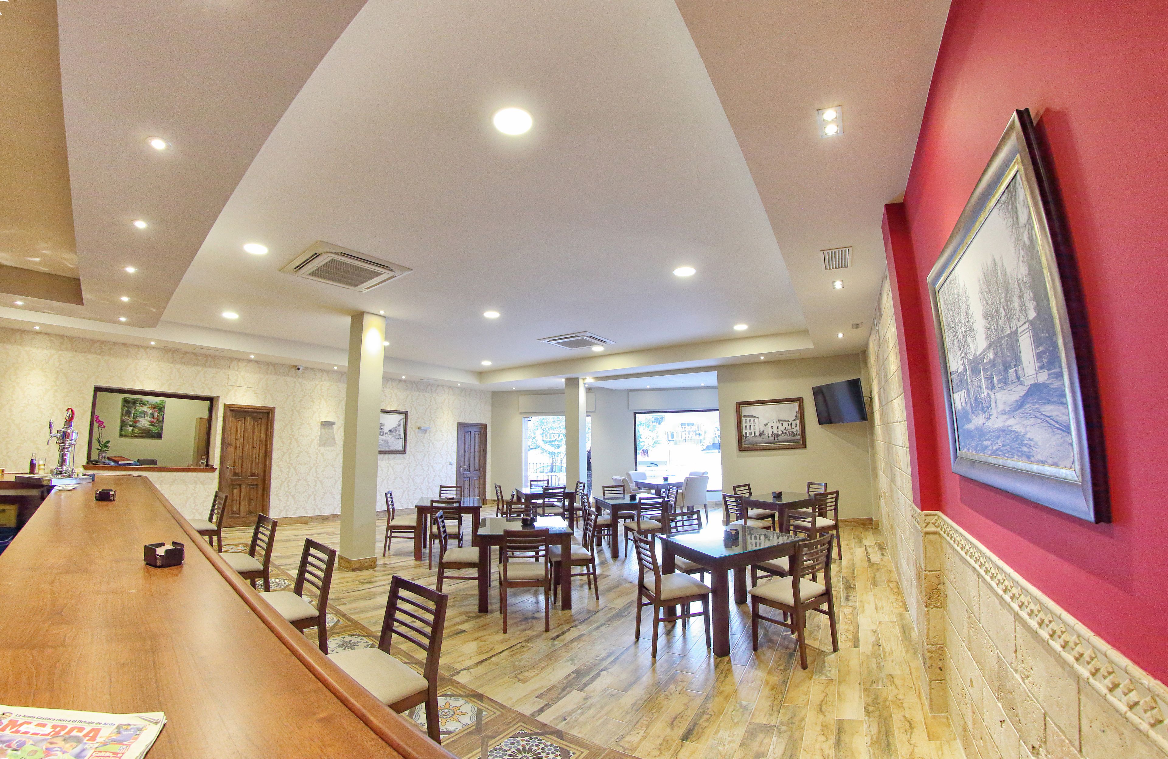 A spacious dining area with multiple tables and chairs, a long wooden counter, and a red accent wall with a framed picture.