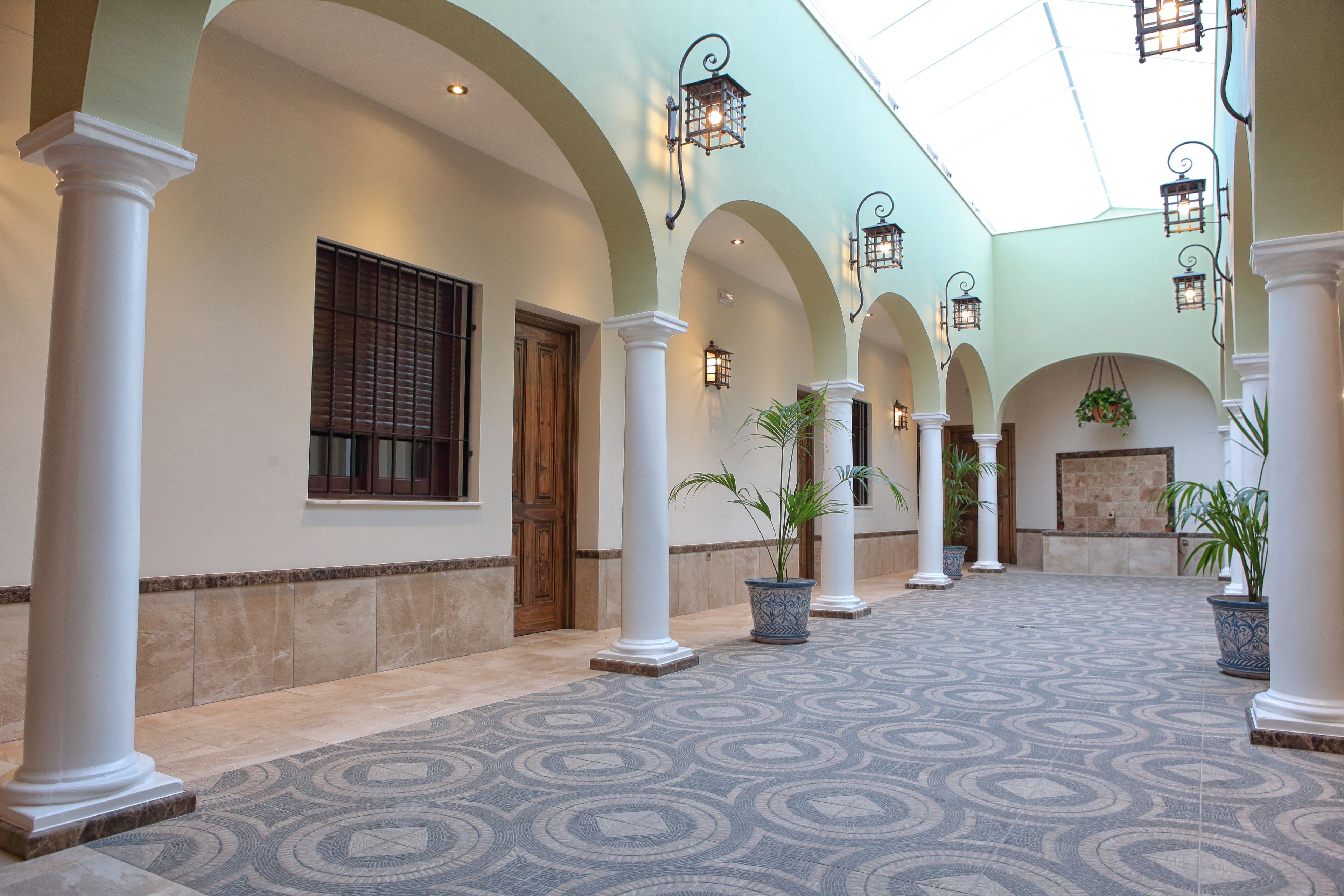A spacious corridor with white columns, patterned floor tiles, and hanging lanterns.