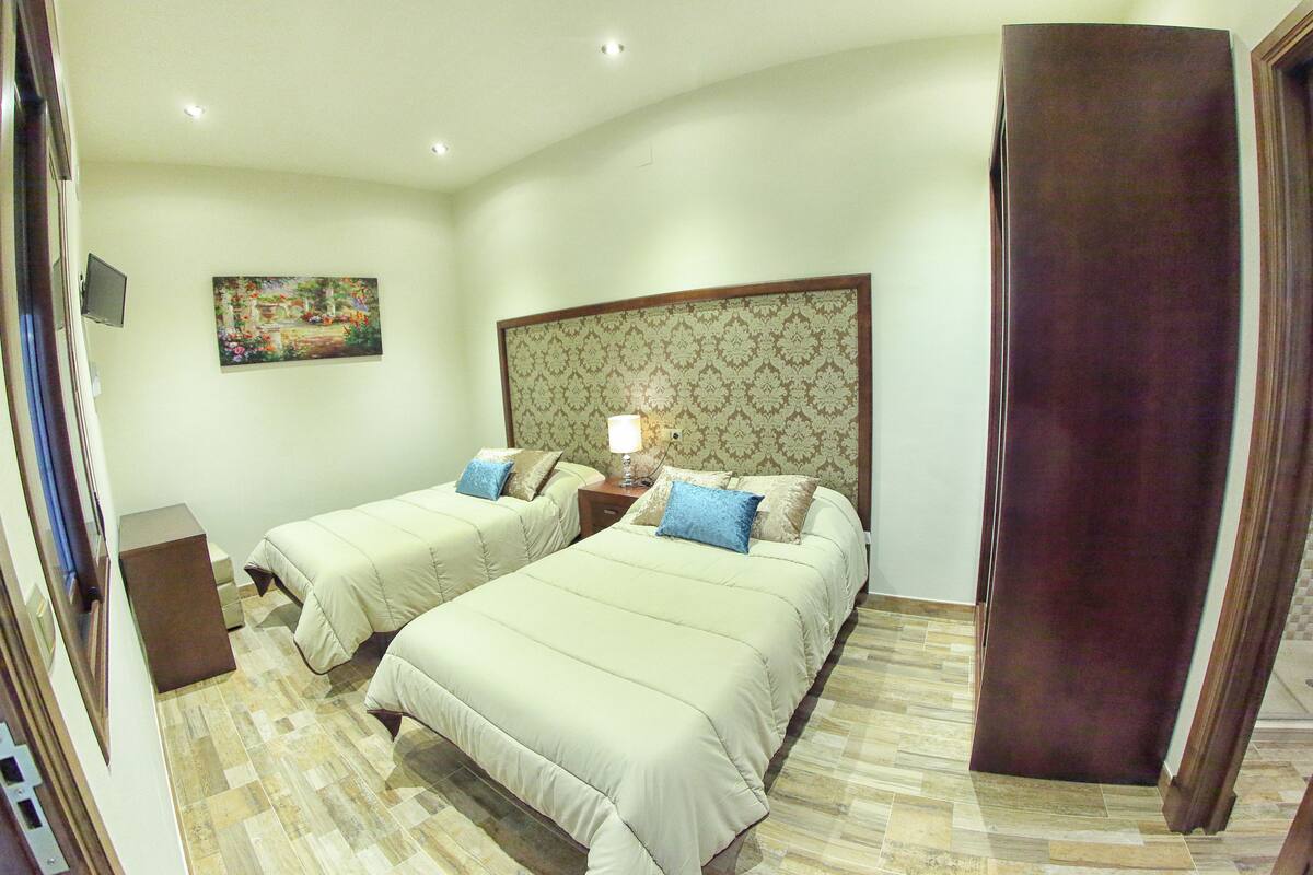 A hotel room with two beds, a television, a painting on the wall, and a patterned headboard.
