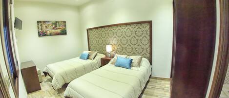 A hotel room with two beds, a television, a painting on the wall, and a patterned headboard.