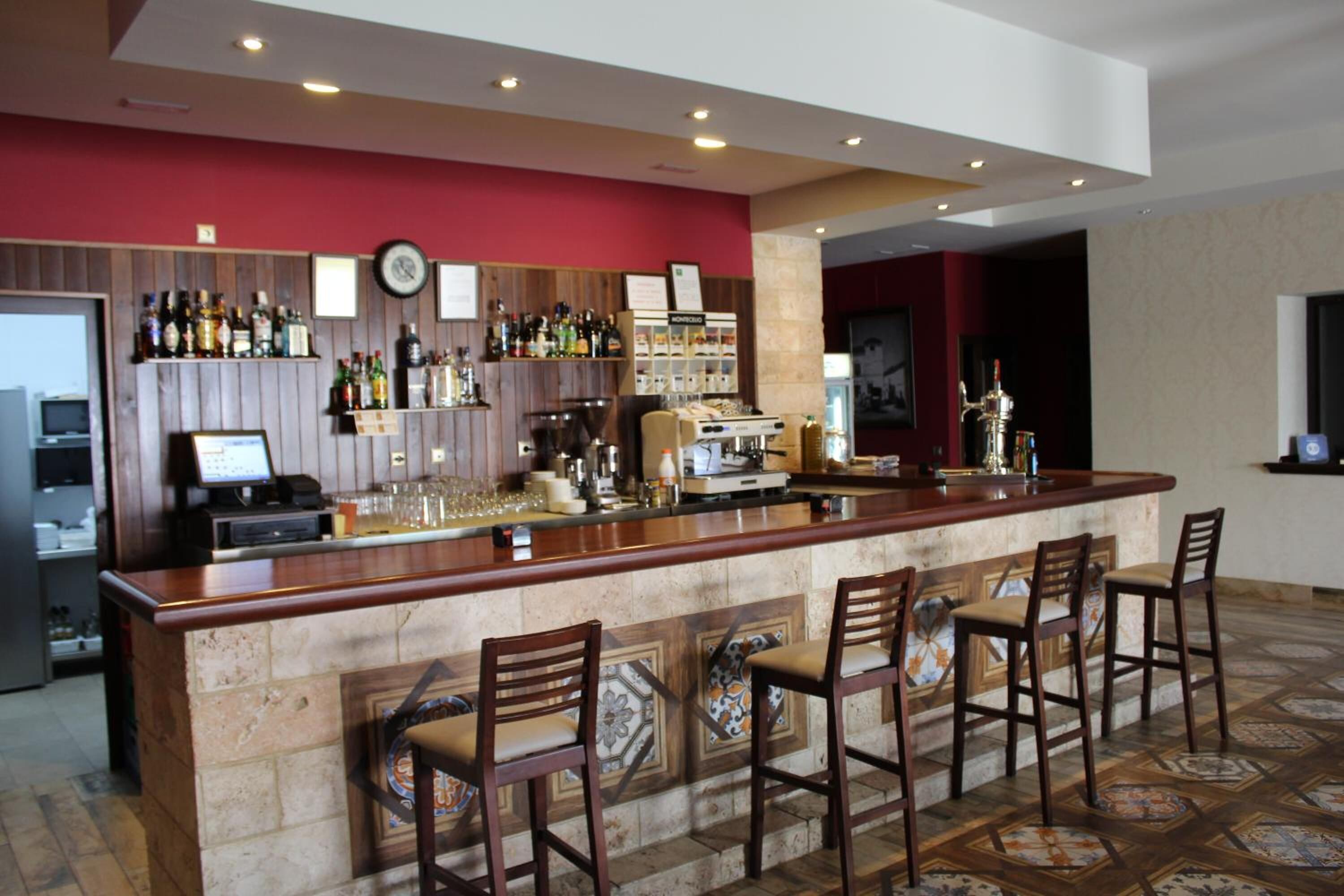 A bar area with a wooden counter, bar stools, and a variety of liquor bottles.