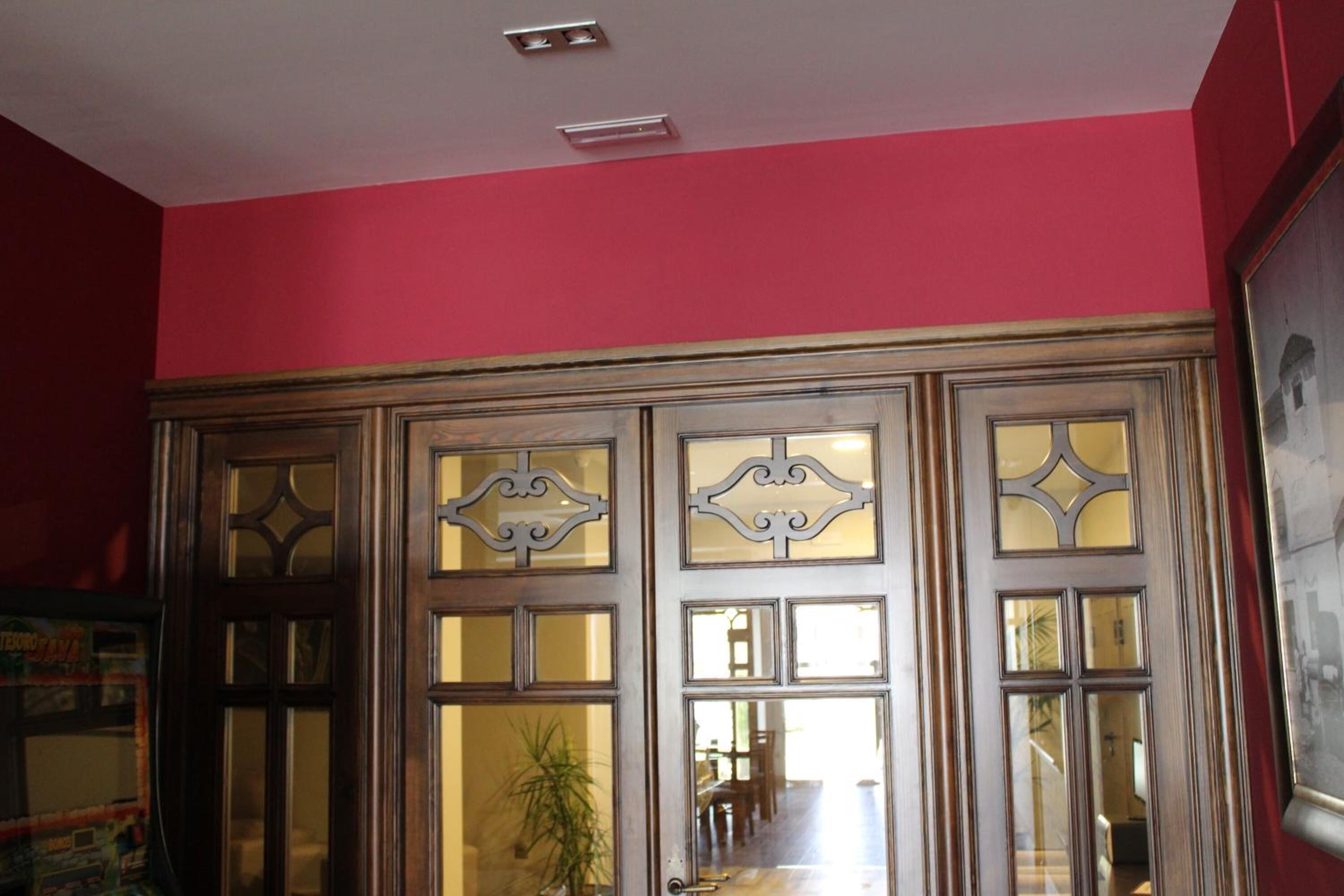 A room with a wooden cabinet with glass doors, a red wall, and a ceiling light fixture.