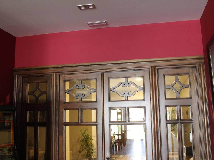 A room with a wooden cabinet with glass doors, a red wall, and a ceiling light fixture.