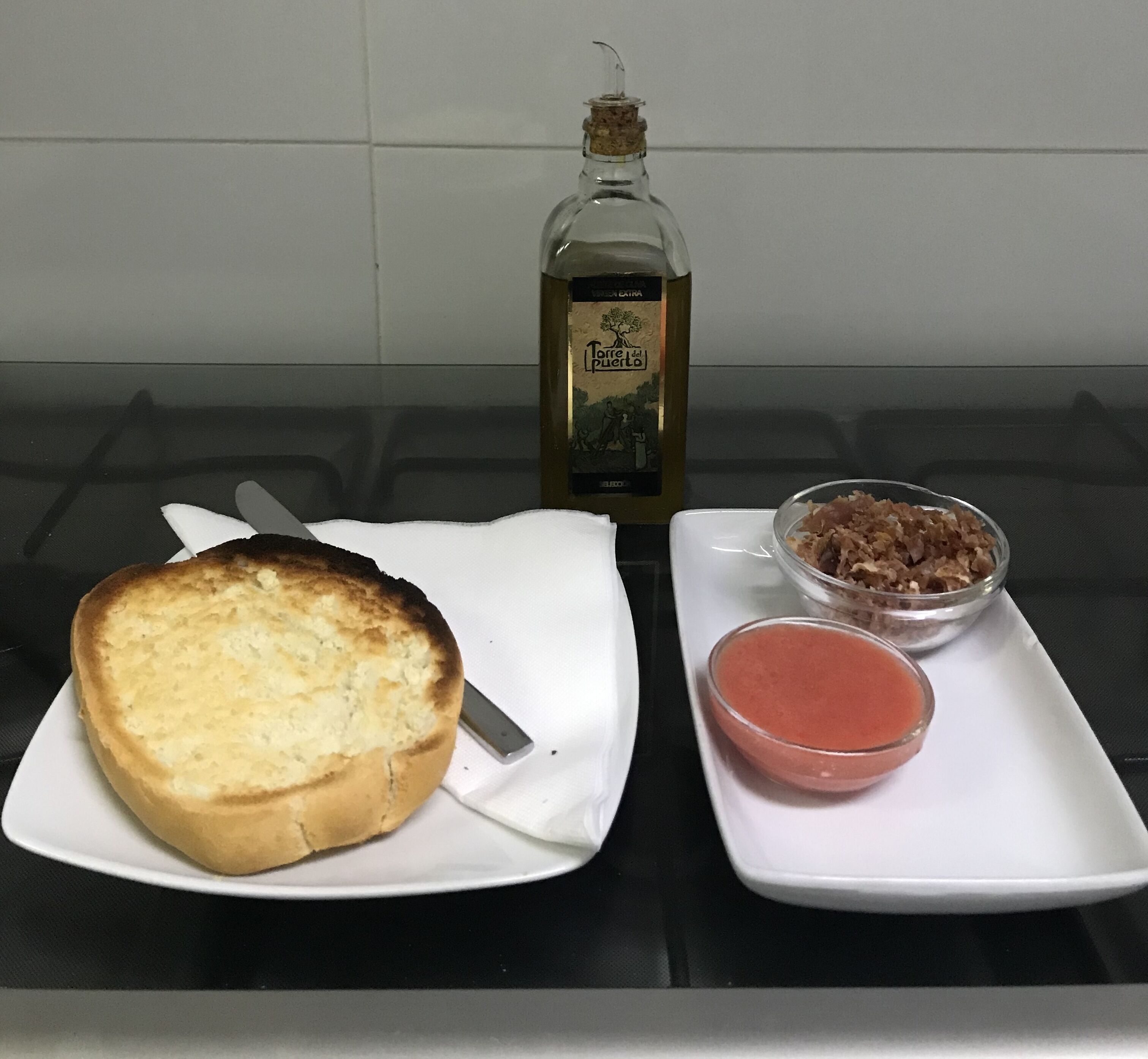 Un plato con un pan tostado, un recipiente pequeño con carne, un tazón de salsa y una botella de aceite de oliva sobre una mesa.