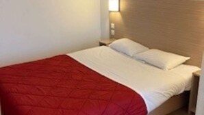 A single bed with a red blanket and white pillows in a room with wooden flooring and a nightstand. - Première Classe Rouen Nord - Bois Guillaume (Bois-Guillaume)