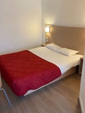 A single bed with a red blanket and white pillows in a room with wooden flooring and a nightstand. - Première Classe Rouen Nord - Bois Guillaume (Bois-Guillaume)