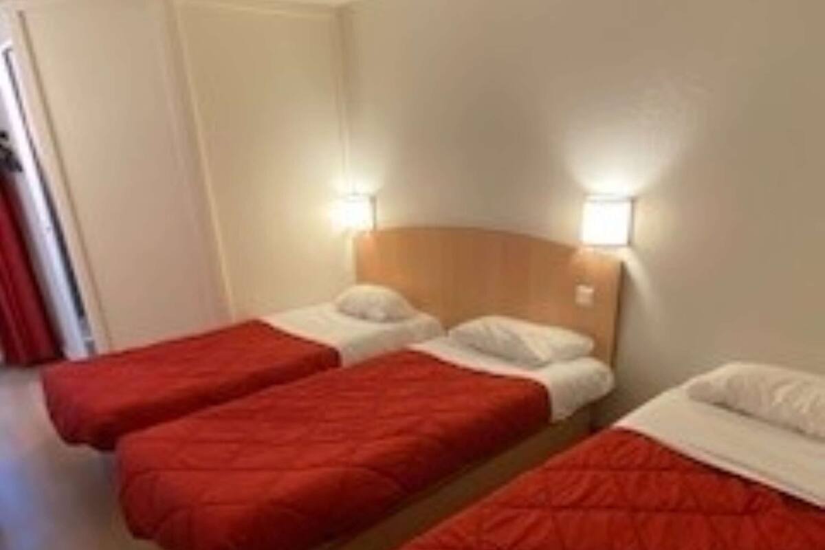 A hotel room with three single beds, each with a red quilted bedspread and white pillows.