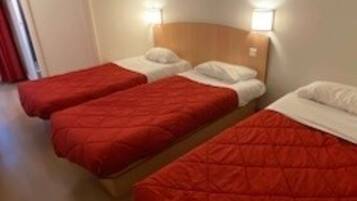A hotel room with three single beds, each with a red quilted bedspread and white pillows.