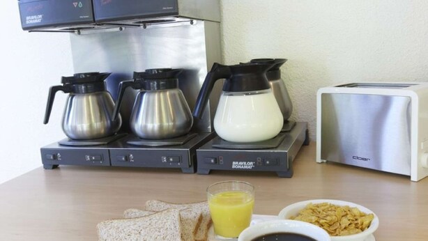 A breakfast setup with a coffee maker, toaster, and a tray with toast, orange juice, coffee, cereal, and a packet of tea. - Première Classe Rouen Nord - Bois Guillaume (Bois-Guillaume)