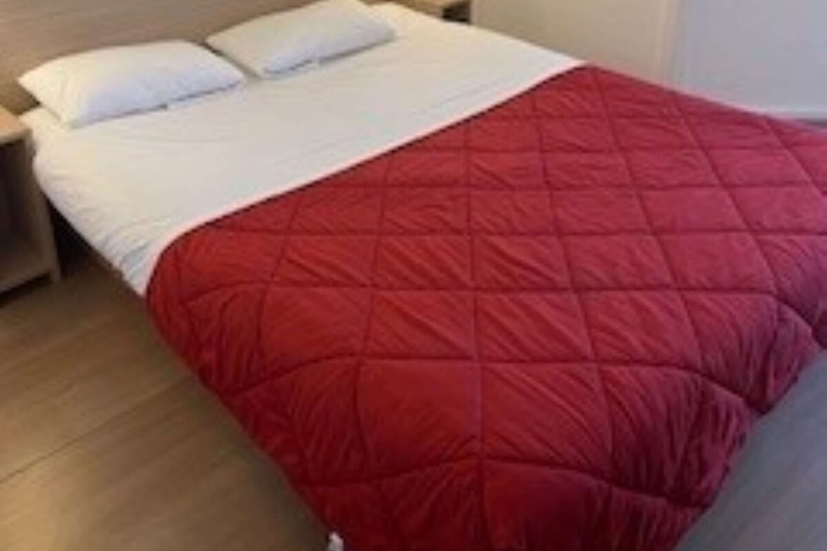 A hotel room with a bed, a nightstand, and a wall-mounted light.