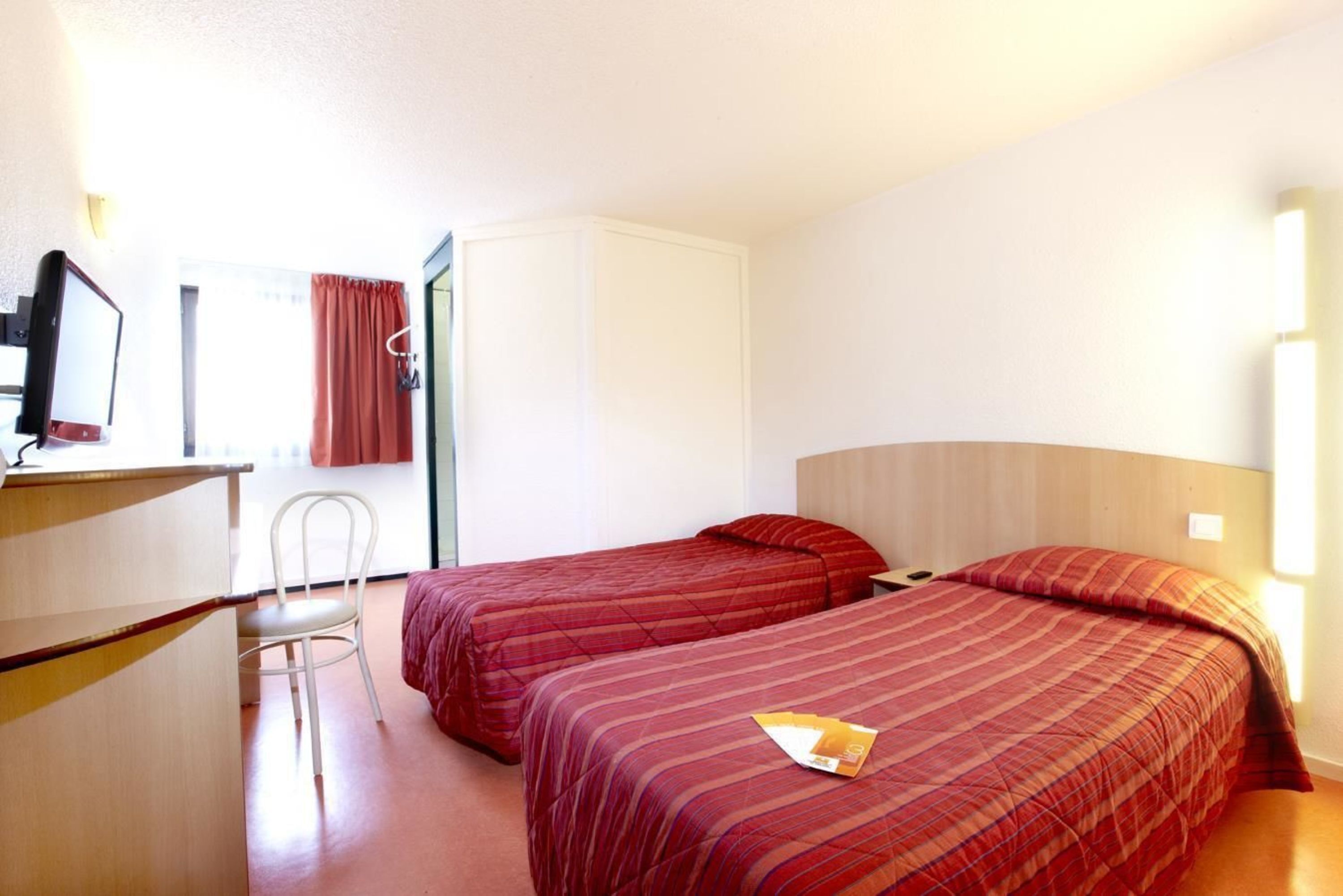 Habitación de hotel con dos camas, un escritorio, una silla y un televisor.