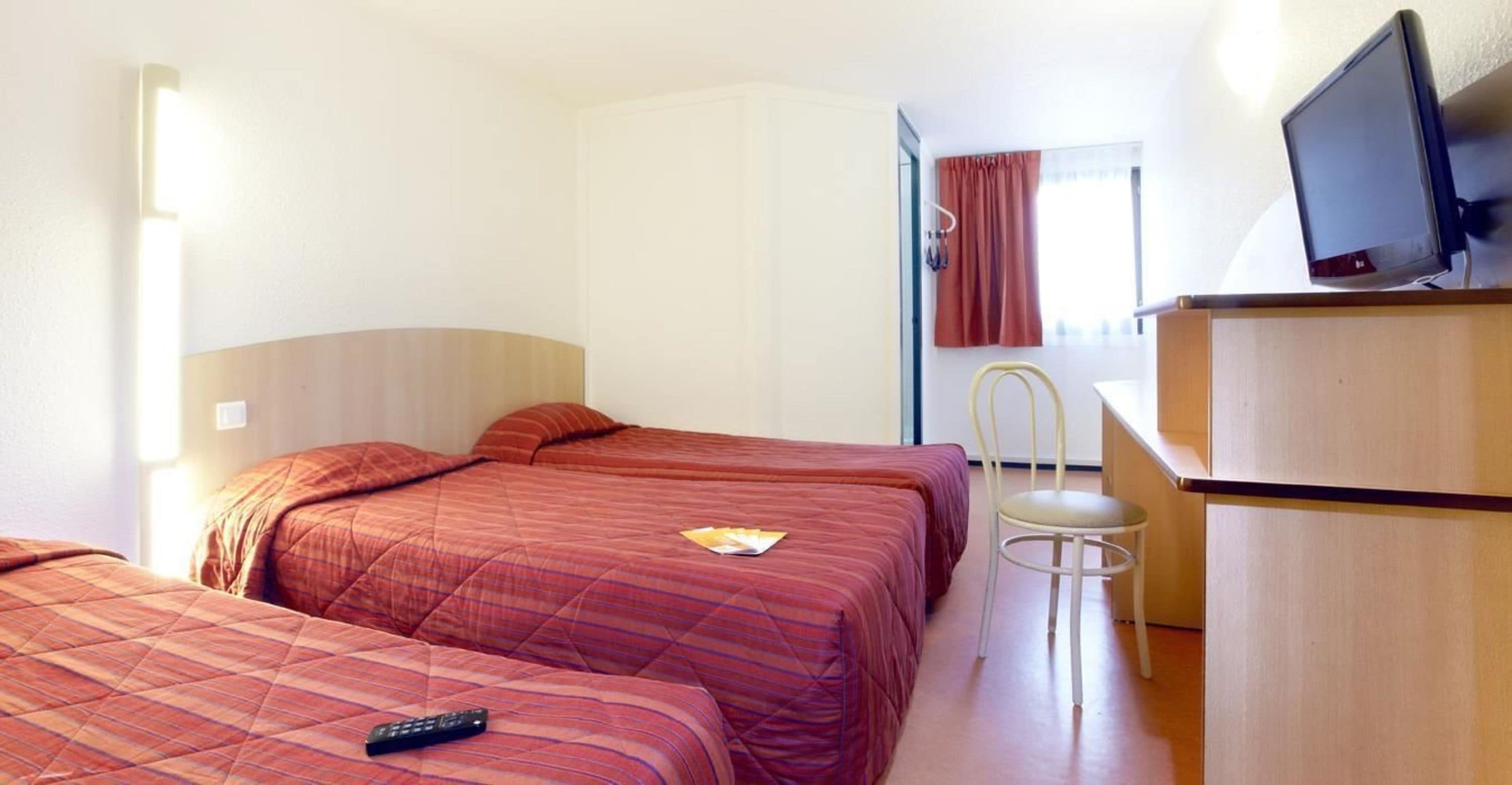 A hotel room with two beds, a desk, a chair, and a television.
