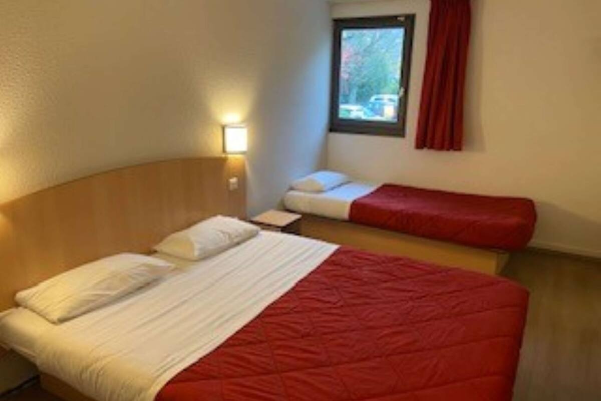 A hotel room with a large bed, a smaller bed, a window with a view, and a red curtain.