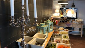 A buffet setup with various food containers, a candelabra with candles, and a television in the background. - Jennys Hotell och Restaurang (Arvika)