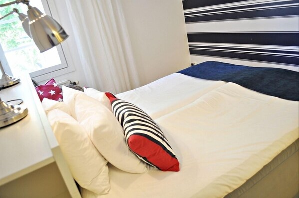A neatly made bed with white and red pillows, a striped pillow, and a blue blanket. - Jennys Hotell och Restaurang (Arvika)