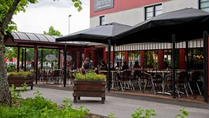 An outdoor seating area with tables and chairs, a wooden planter with flowers, and a building with a sign reading "Jennys". - Jennys Hotell och Restaurang (Arvika)