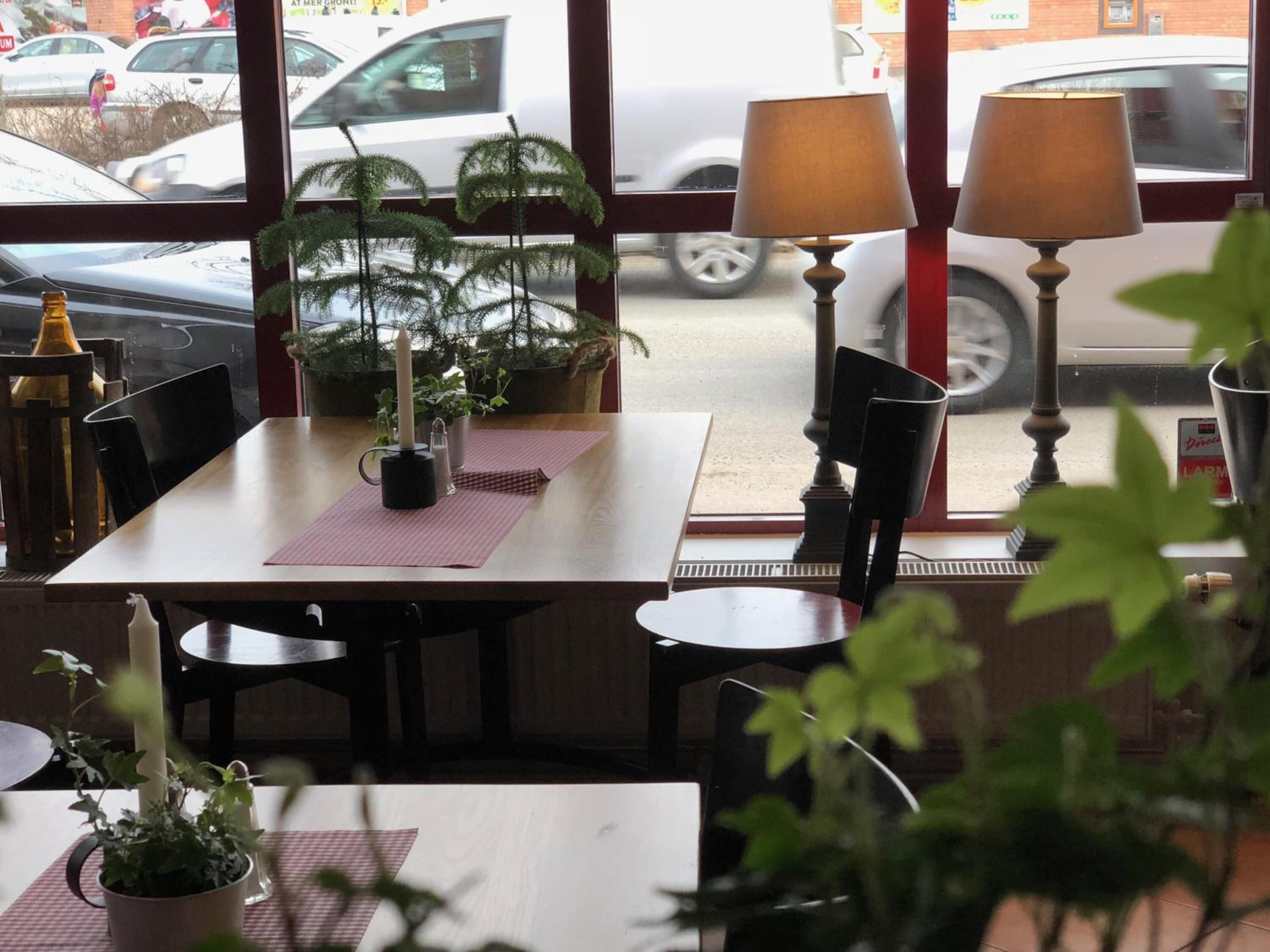 A restaurant interior with a table set for two, two chairs, a potted plant, a candle, and two table lamps.