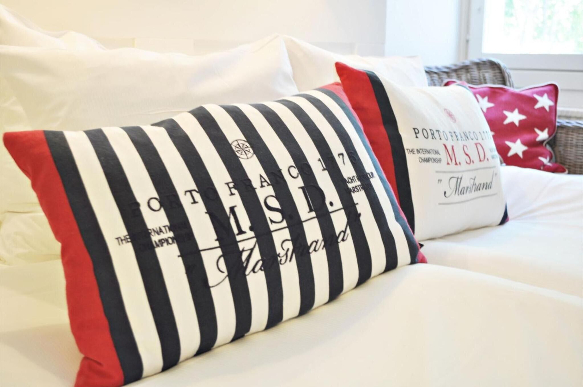 A bed with white bedding and striped pillows, one with text and another with a logo.