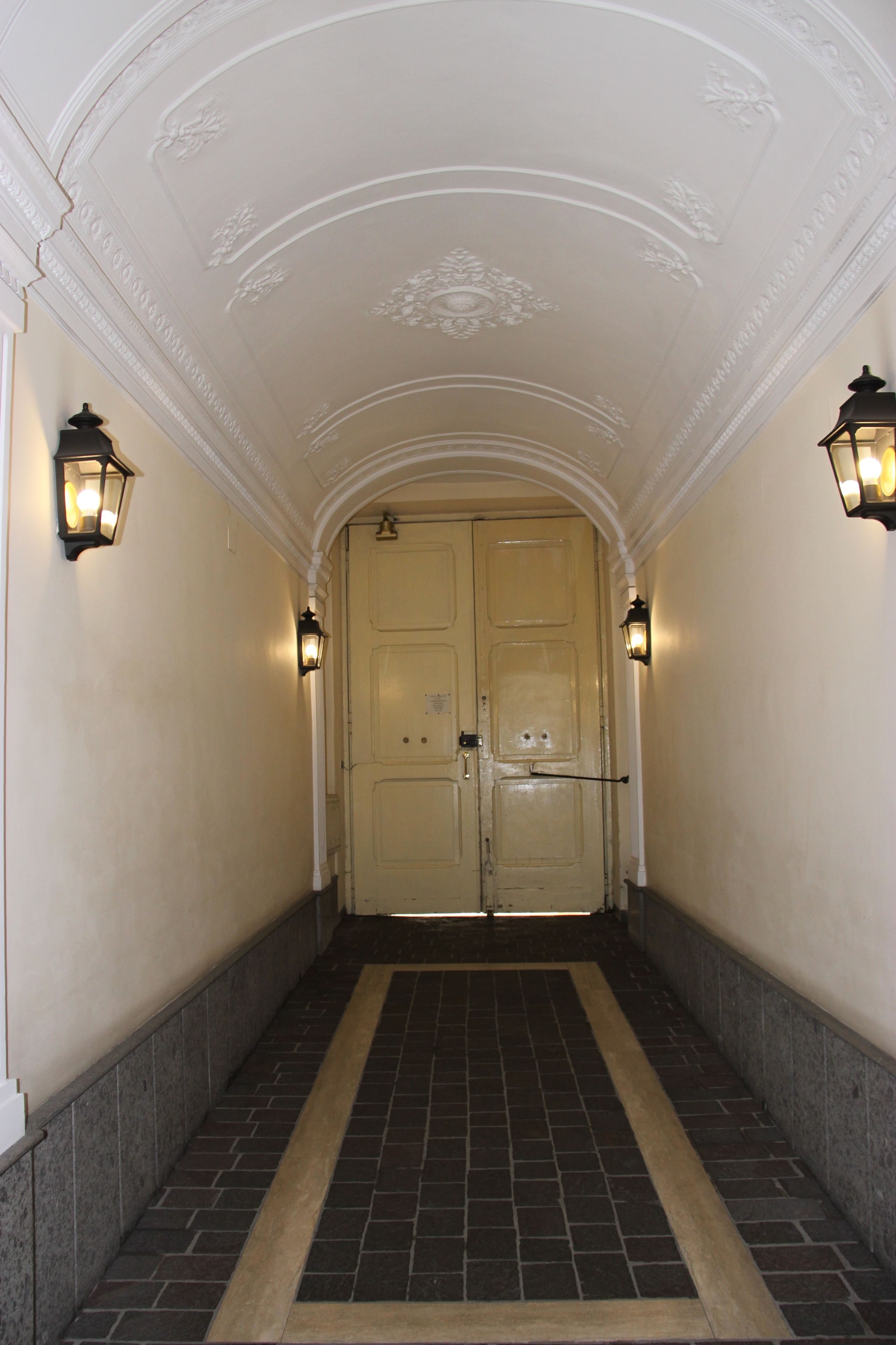 A hallway with a double door, two wall-mounted lights, and a patterned floor.
