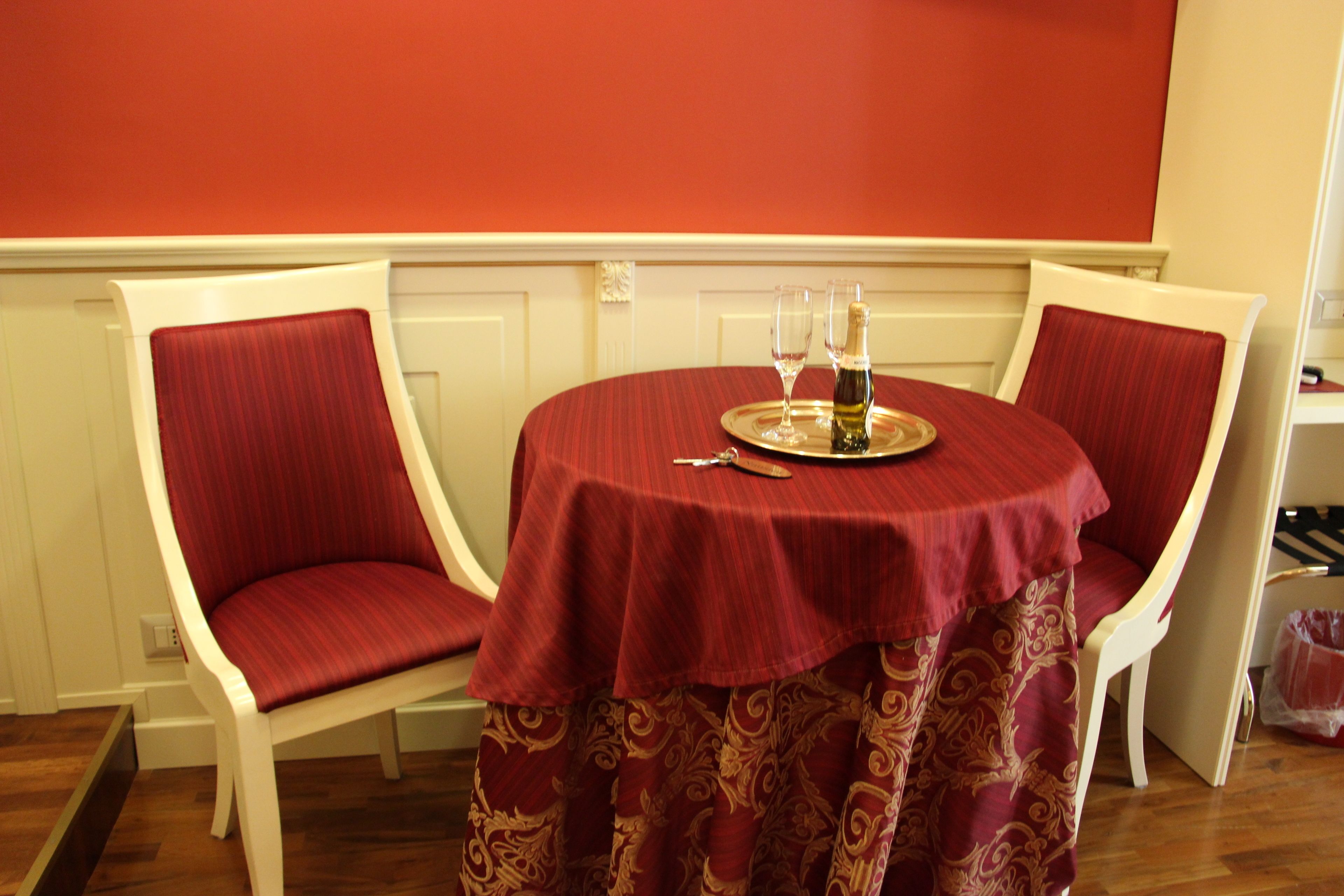 Une table à manger recouverte d’une nappe rouge, deux chaises à l’assise rouge et une bouteille de champagne posée sur un plateau.