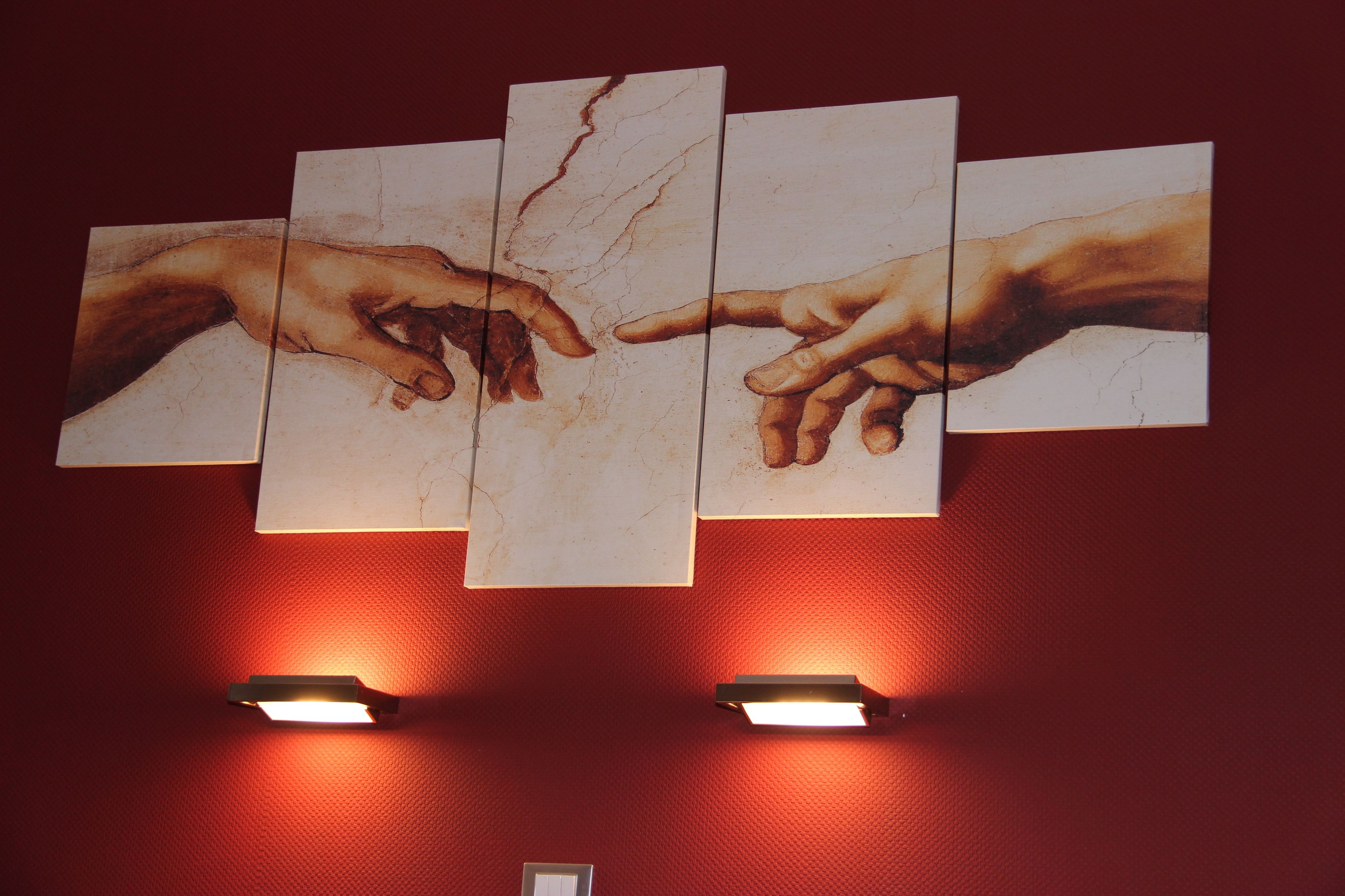 Pared con una obra de arte de manos extendiéndose la una hacia la otra, flanqueada por dos luces empotradas.