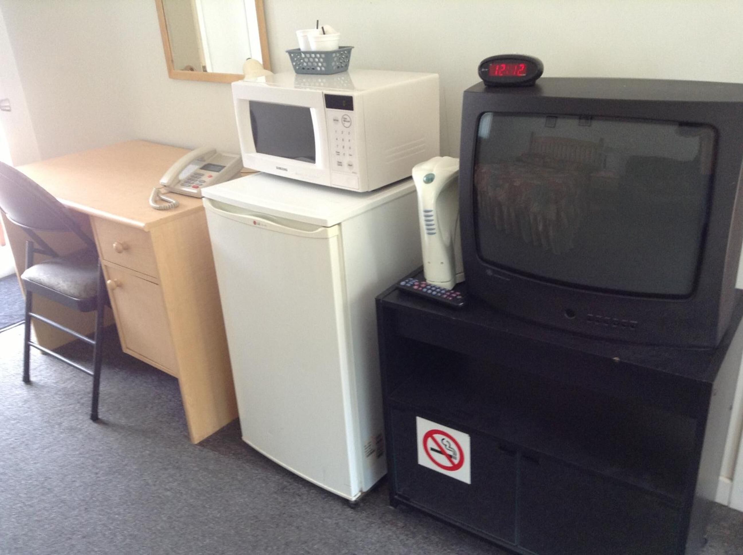 A compact kitchenette with a microwave, refrigerator, and a television on a stand.