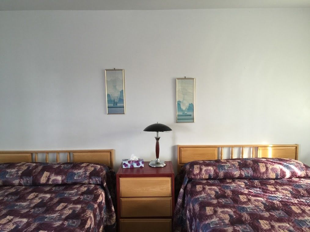 A hotel room with two beds, a nightstand with a lamp, and two framed pictures on the wall.