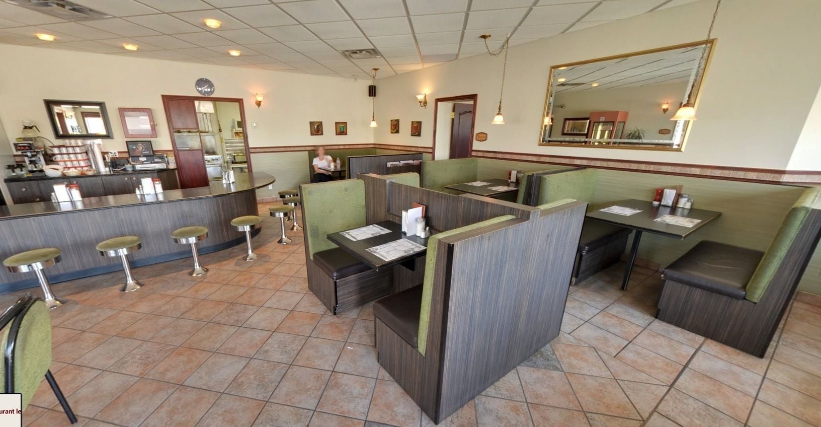 Un interior de restaurante con cabinas, mesas altas y una barra.