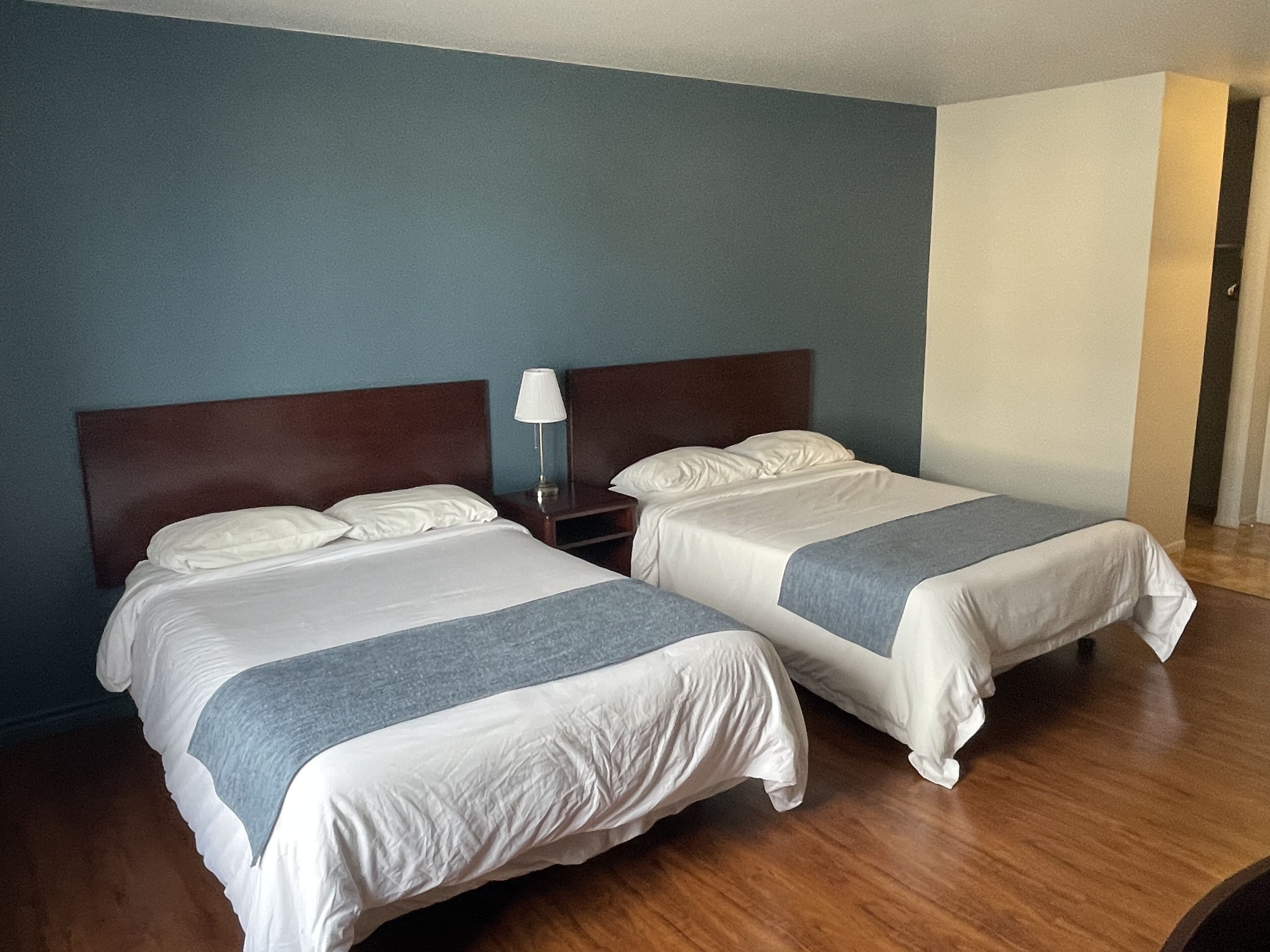 Dos camas individuales con cabeceros de madera, ropa de cama blanca y un detalle gris al pie de cada cama.