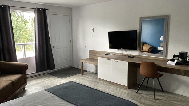 Una habitación de hotel con cama, escritorio, computadora, televisor y una silla.