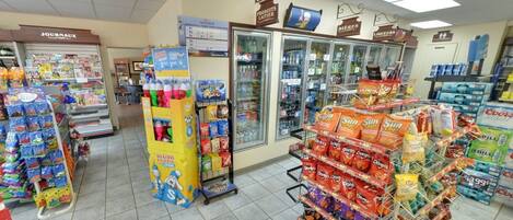 Interior de un supermercado con una variedad de productos en estantes y congeladores, incluyendo aperitivos, bebidas y productos lácteos.