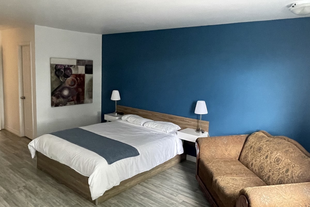 A hotel room with a bed, two bedside tables, a nightstand, a couch, and a painting on the wall.