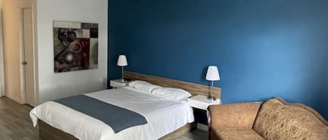 Une chambre d’hôtel avec un lit, deux tables de chevet, une petite table, un canapé et un tableau au mur.