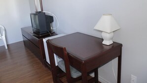 Una habitación pequeña con una mesa de madera, una silla, un televisor sobre un mueble y una lámpara.