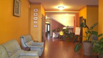 A hotel lobby with a reception desk, a staircase, and a seating area with two sofas.