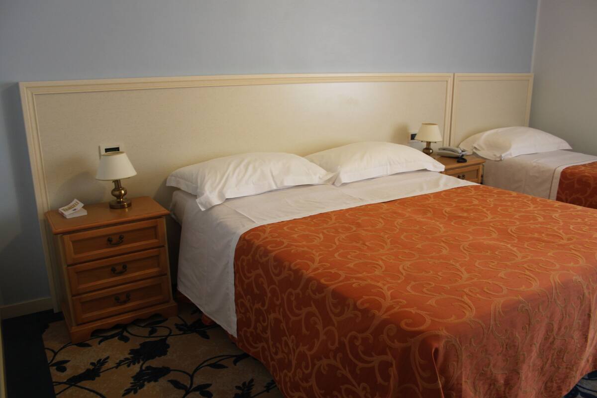 A hotel room with two beds, a nightstand with a lamp, and a telephone.