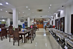 A cafeteria with multiple dining tables and chairs, a buffet line with various food containers, and a counter area with a beverage dispenser. - KMA 115 Miles Hotel (Phyu)