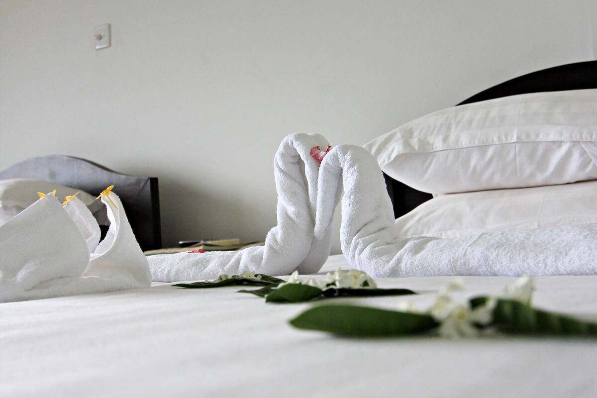 Una cama bien hecha con sábanas blancas, cabecera negra y una lámpara de pared.
