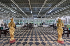 Un amplio espacio interior con piso a cuadros, dos estatuas doradas y mesas y sillas dispuestas para comer.