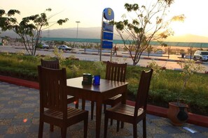 An outdoor seating area with a table and chairs, a signpost in the background, and a view of a road and distant mountains. - KMA 115 Miles Hotel (Phyu)