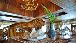 Une table de salle à manger en bois ornée d’un élément décoratif sculpté représentant un lion, un vase avec une plante et un cloche en verre transparent.