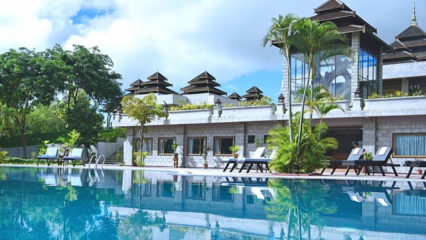 Un hôtel doté d’une piscine, de chaises longues et présentant des éléments architecturaux traditionnels.