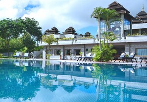 Un hotel con piscina, sillones de descanso y elementos arquitectónicos tradicionales.