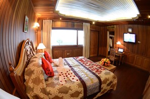 Habitación de hotel con una cama grande, cabecera de madera, un escritorio con computadora, televisor en la pared y una ventana con cortinas.
