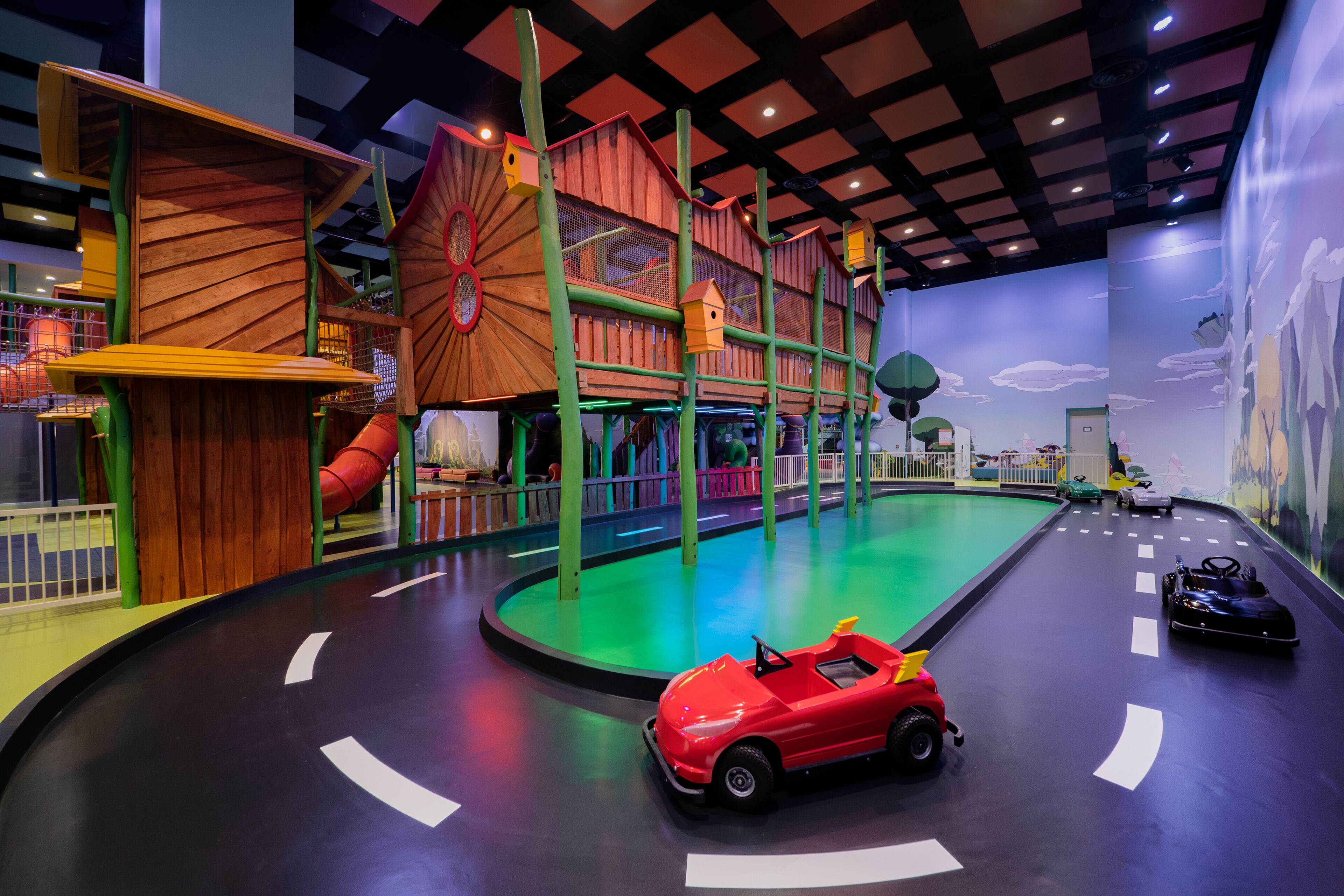 Een kinderspeelplaats met een houten klimstructuur, een glijbaan en een racebaan met speelgoedauto's.