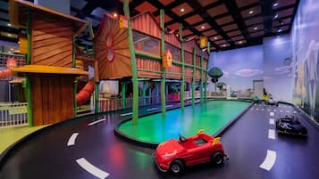 Een kinderspeelplaats met een houten klimstructuur, een glijbaan en een racebaan met speelgoedauto's.