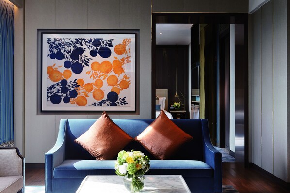 A modern living room with a blue sofa, two brown cushions, and a vase of flowers on a marble coffee table. - Studio City (Cotai)