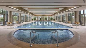 Una amplia piscina interior con un jacuzzi central, rodeada de zonas de estar y grandes ventanales.