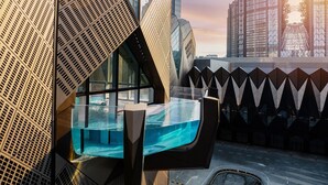 En modern inredning med en vägg som har ett geometriskt mönster, en pool med glasväggar och utsikt över höga byggnader.