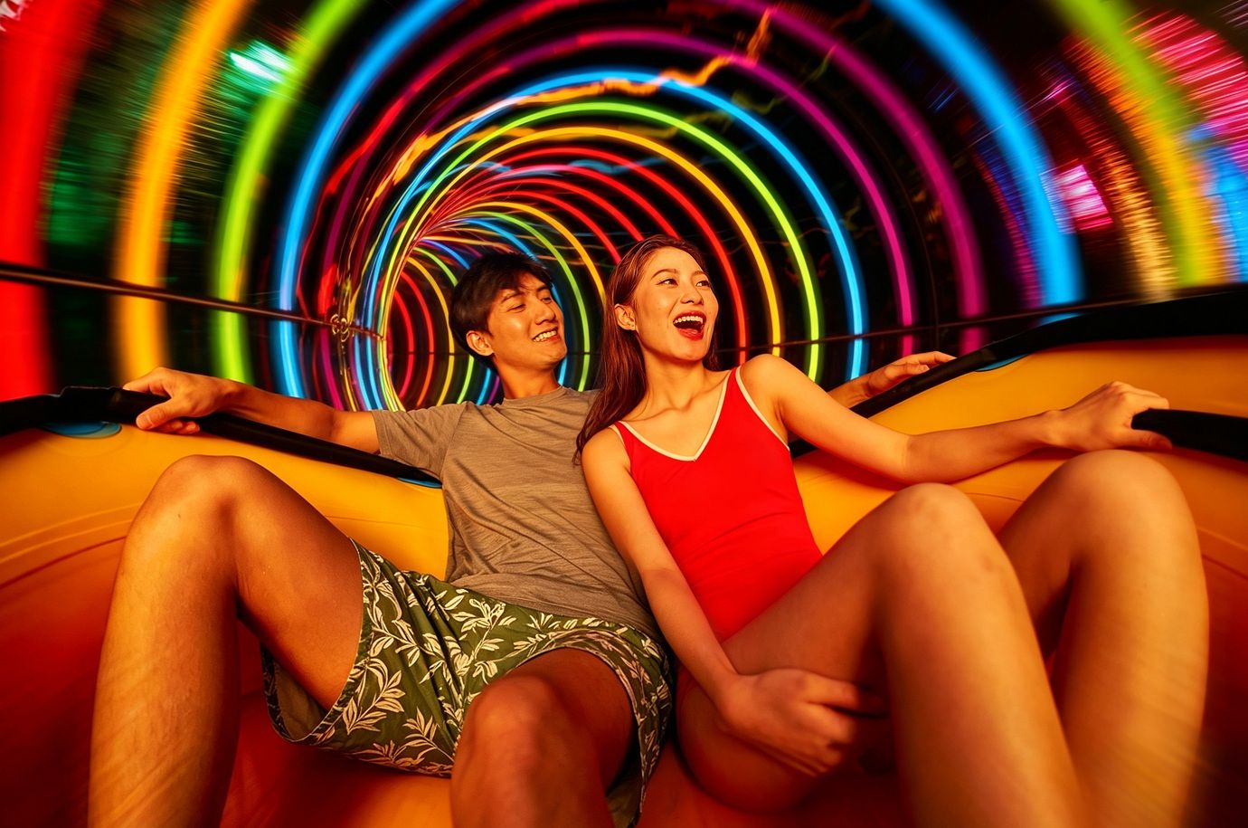 Duas pessoas sentadas numa superfície curva com uma instalação de luz circular e colorida ao fundo.